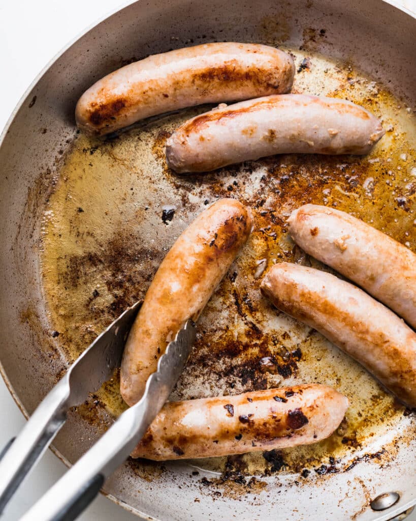Turning the seared bangers in the skillet with a pair of tongs.