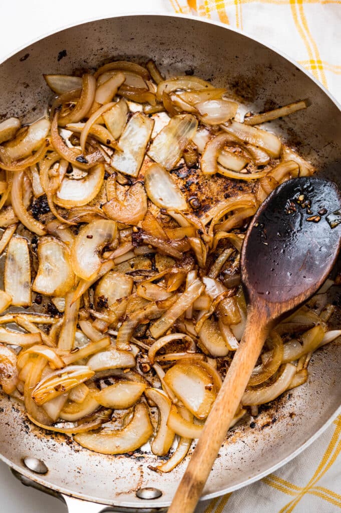 Sauteing onions in the same skillet as the sausages. The onions are tender with a golden color.