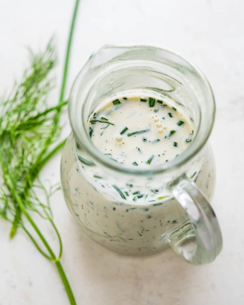 A small glass pitcher filled with the creamy buttermilk herb dressing recipe.