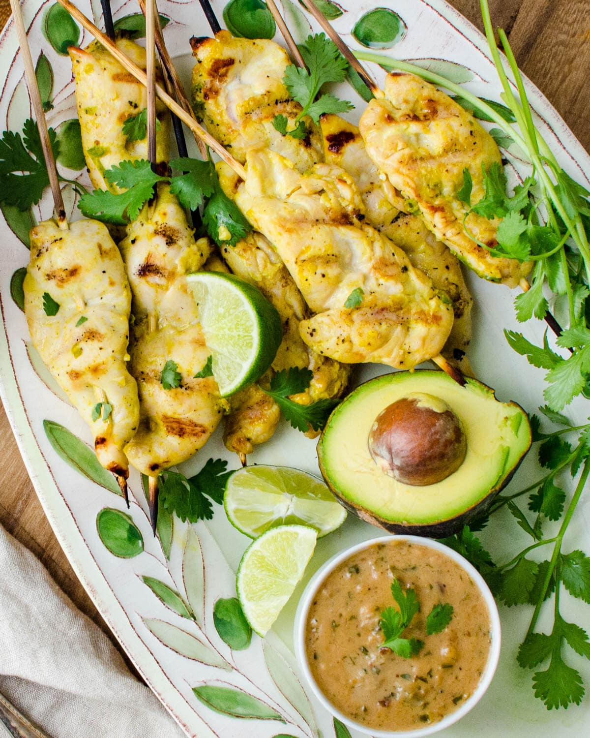 Serving the cooked chicken skewers on a platter with peanut sauce, extra cilantro, lime and avocado.