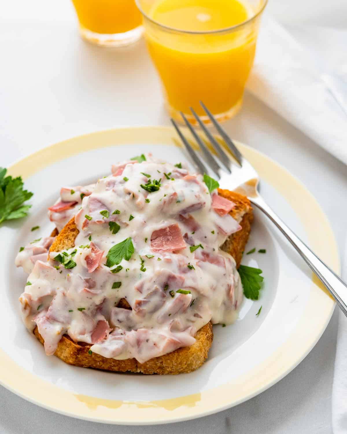 A plate of creamed chipped beef on a slice of toast with a glass of orange juice.