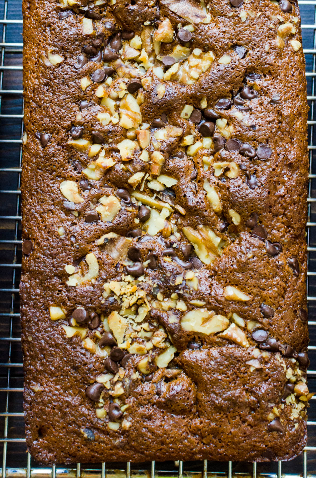 A loaf of baked banana bread with chocolate chips and walnuts cooling on a rack.