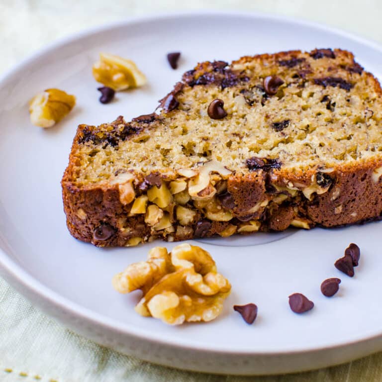 A slice of the banana bread recipe on a plate with sprinkles of chocolate chips and walnuts.