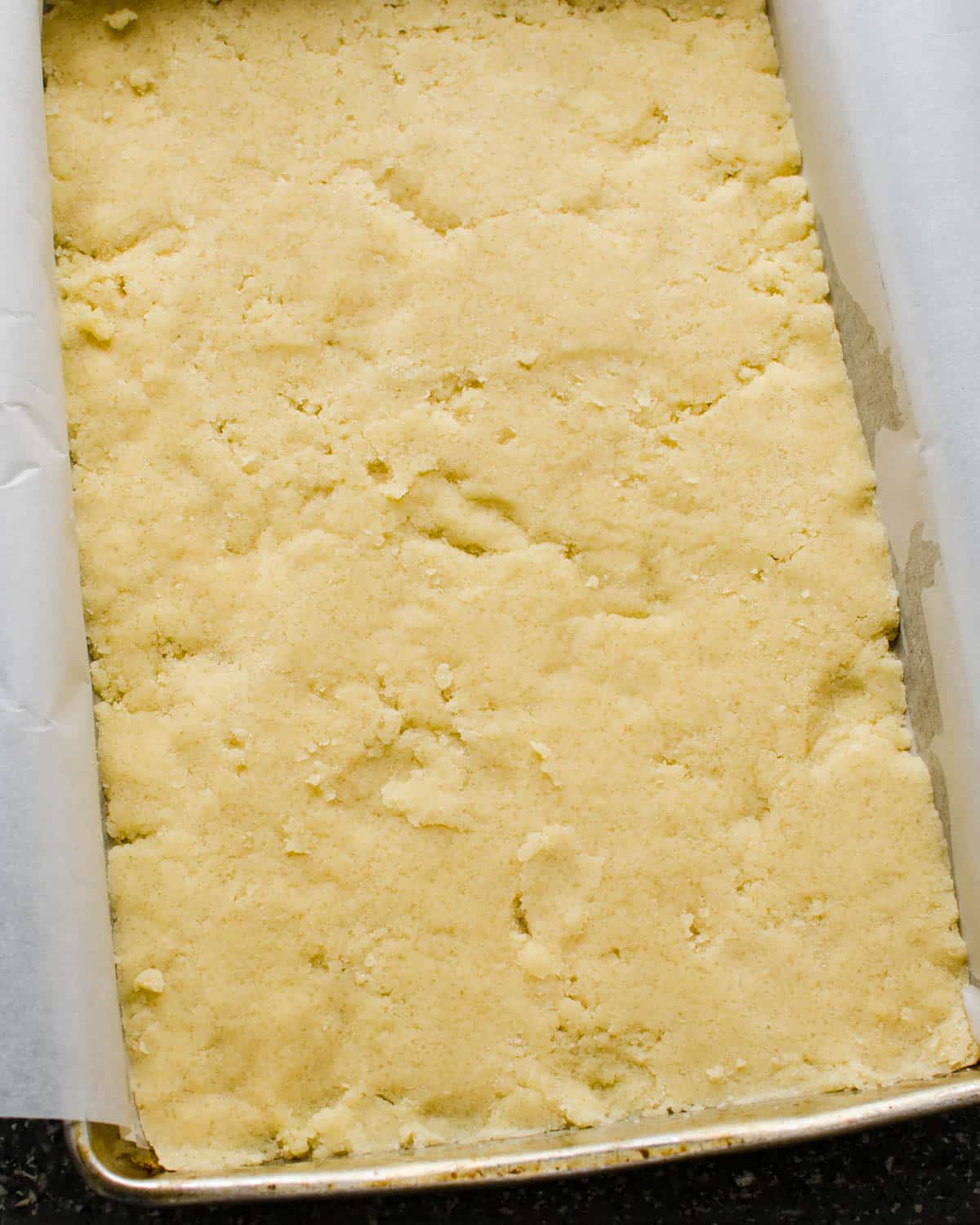 Pressing the shortbread crust into the prepared baking pan.