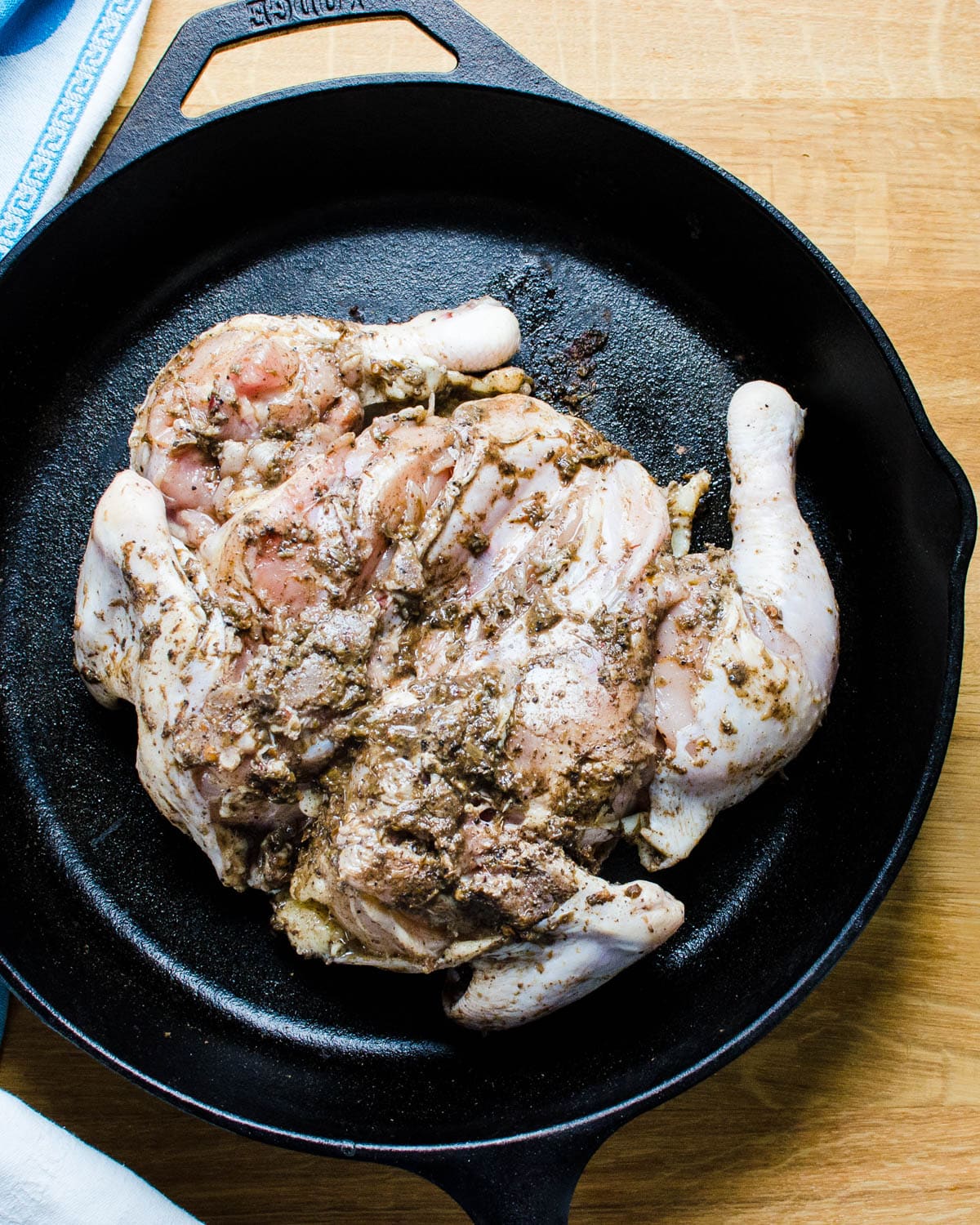 Placing the seasoned spatchcock chicken in a hot cast iron skillet.