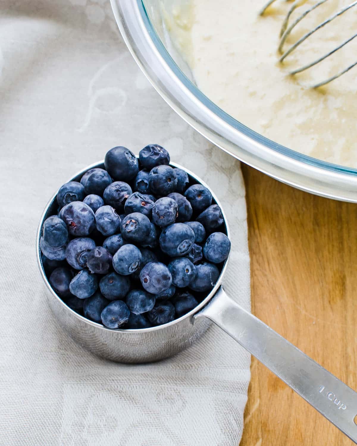 A cup of fresh blueberries next to the batter.