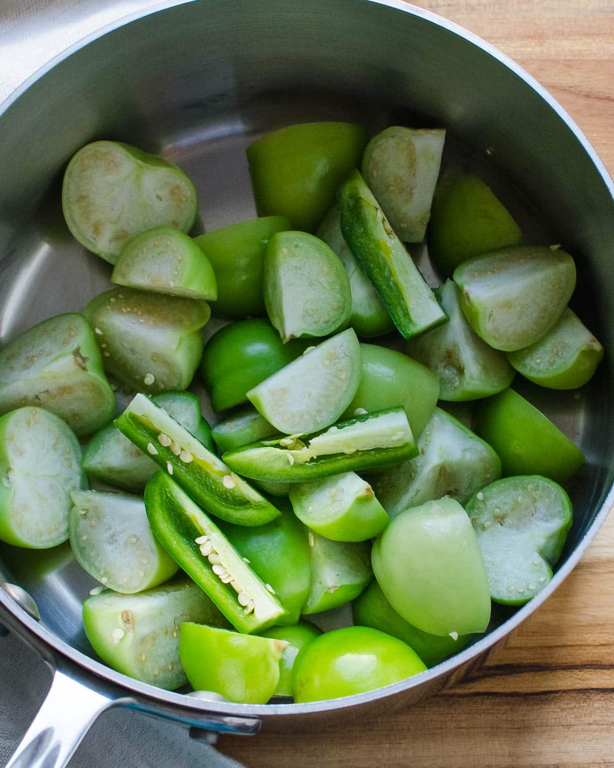 Chopped tomatillos and jalapenos in a saucepan.