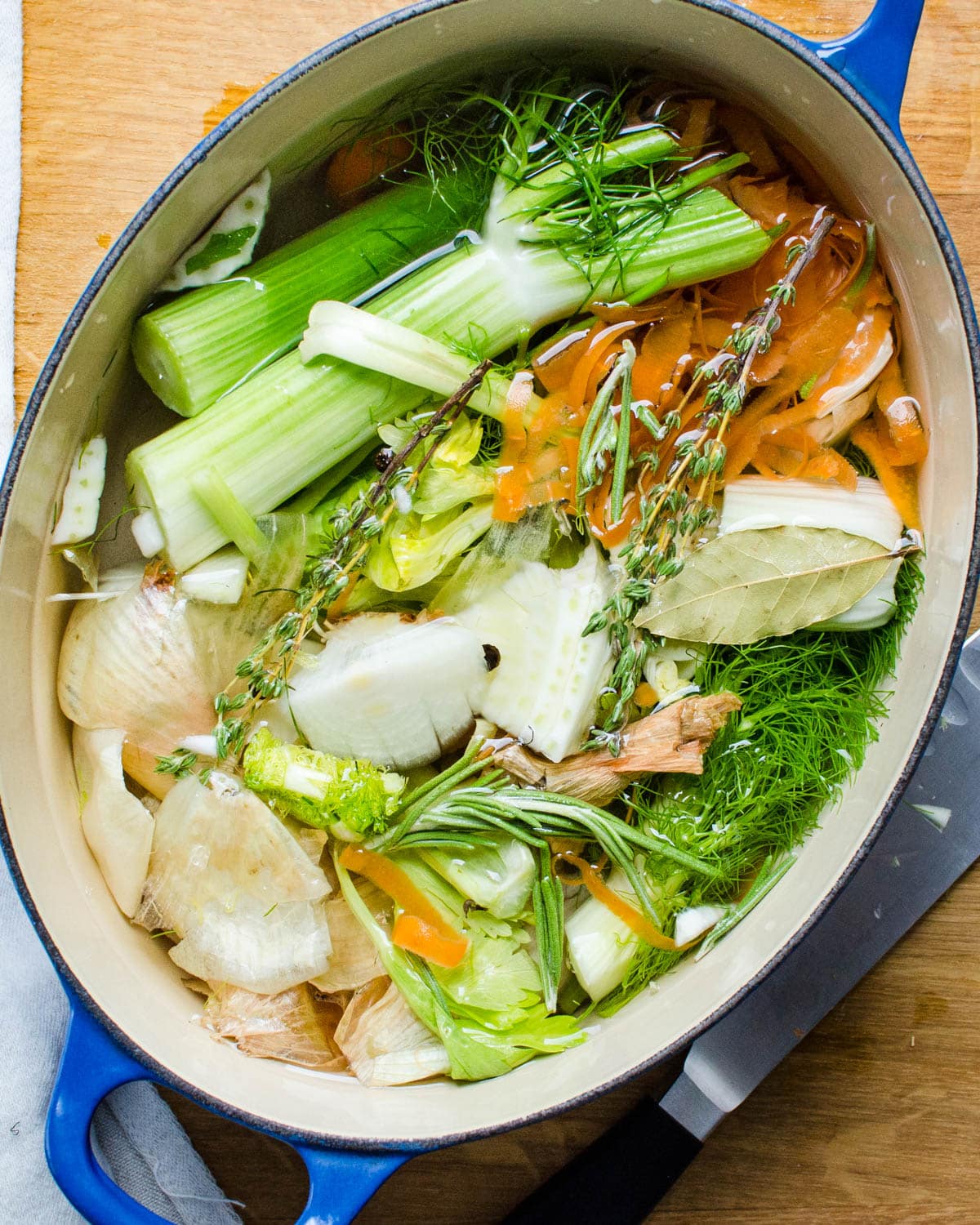 A pot is full of vegetable scraps, aromatics and fresh water.