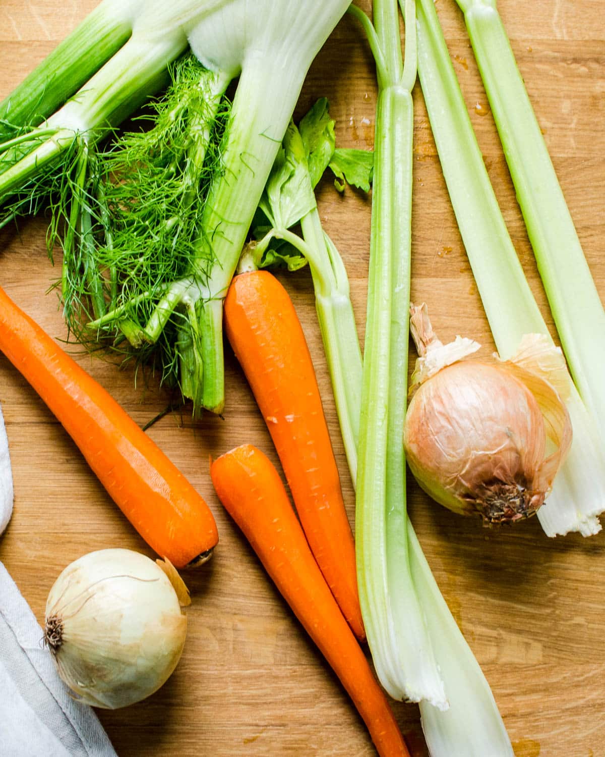 Fennel, carrots, celery and onion on a cutting board.