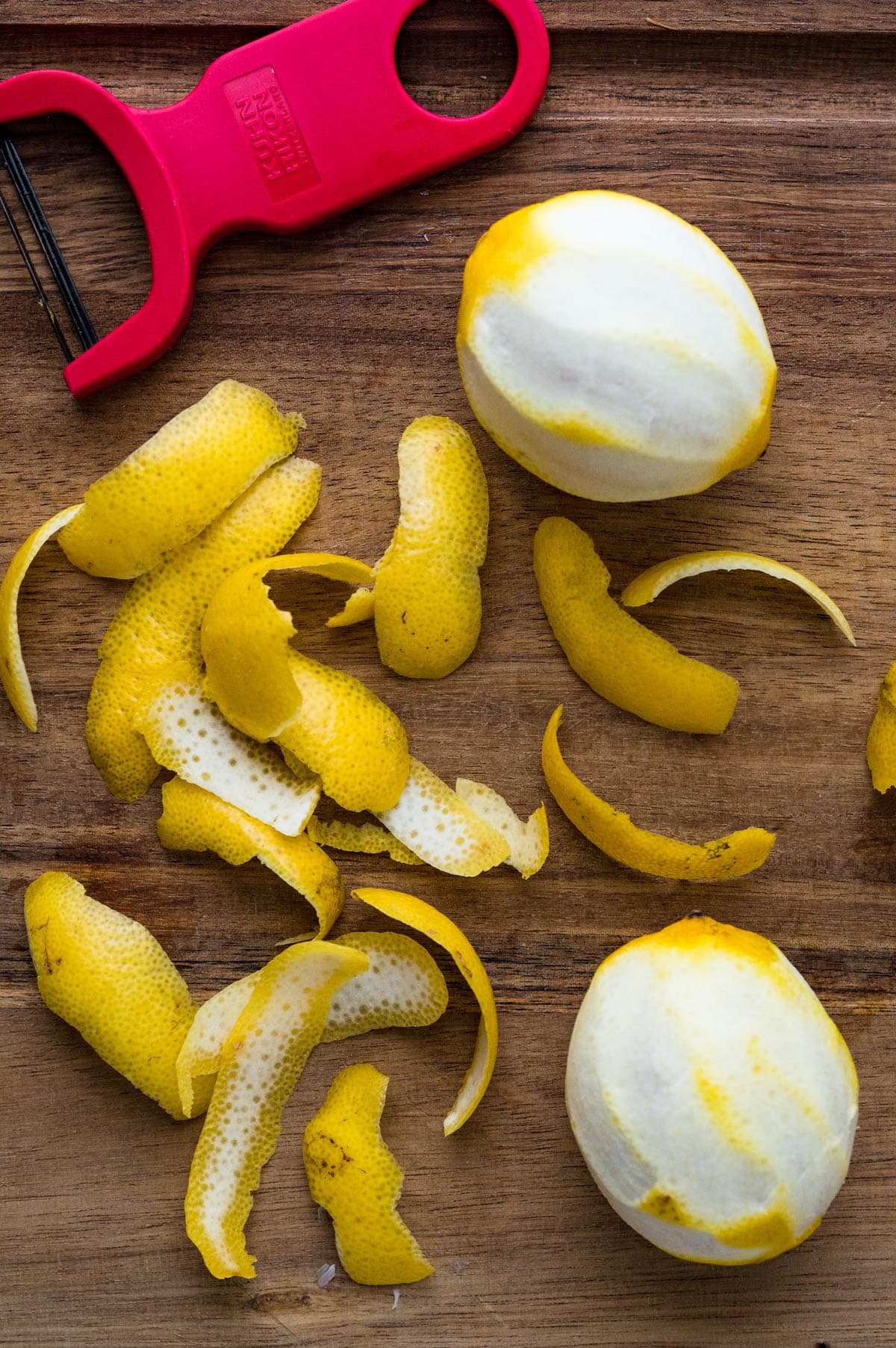 Using a vegetable peeler to remove strips of lemon zest from the fruit.