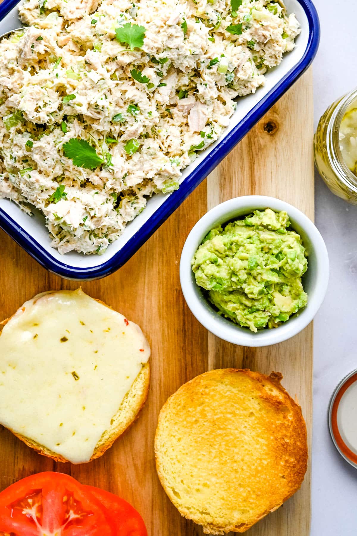 Ingredients for the ultimate tuna salad sandwich are spicy tuna fish salad, mashed avocado, melty pepper jack cheese and pickles on a brioche bun.