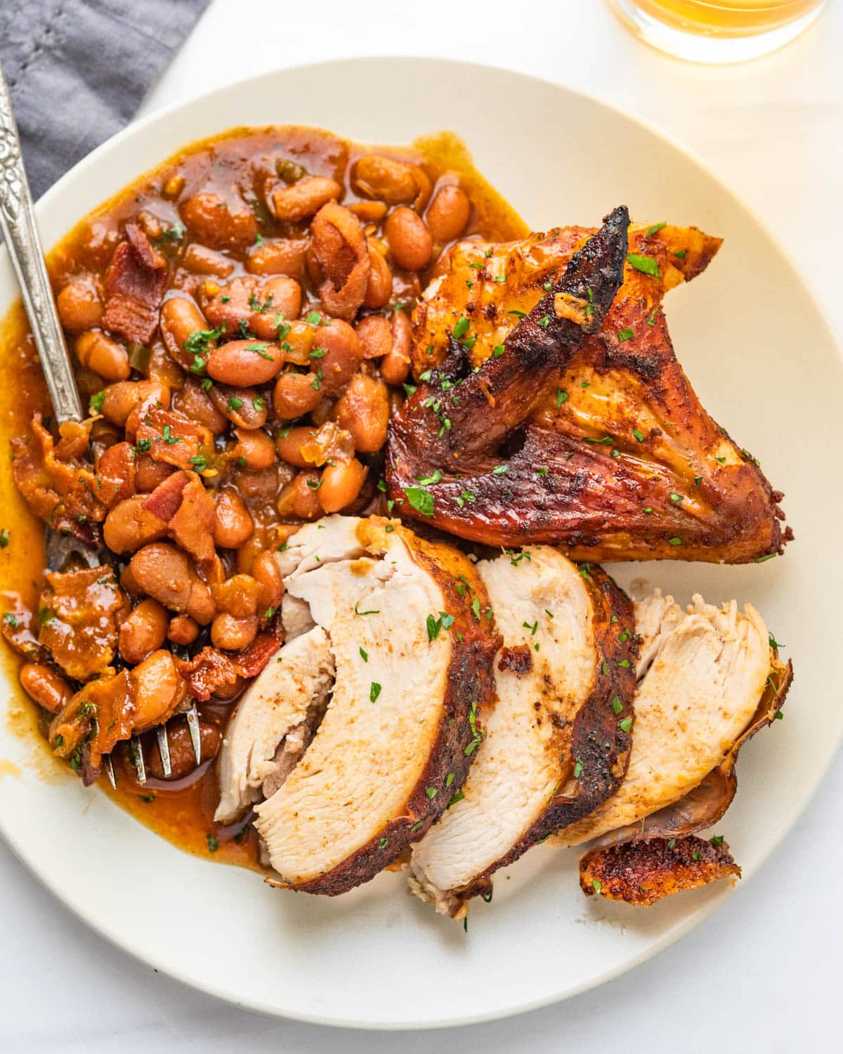 A plate of chicken breast and wing with baked beans on the side.