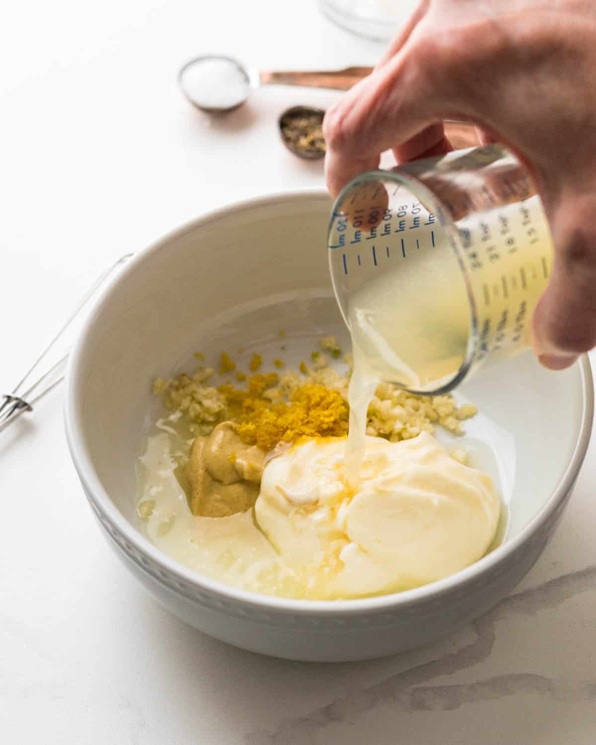 Combining lemon juice with garlic, dijon, lemon zest and mayonnaise in a small bowl.