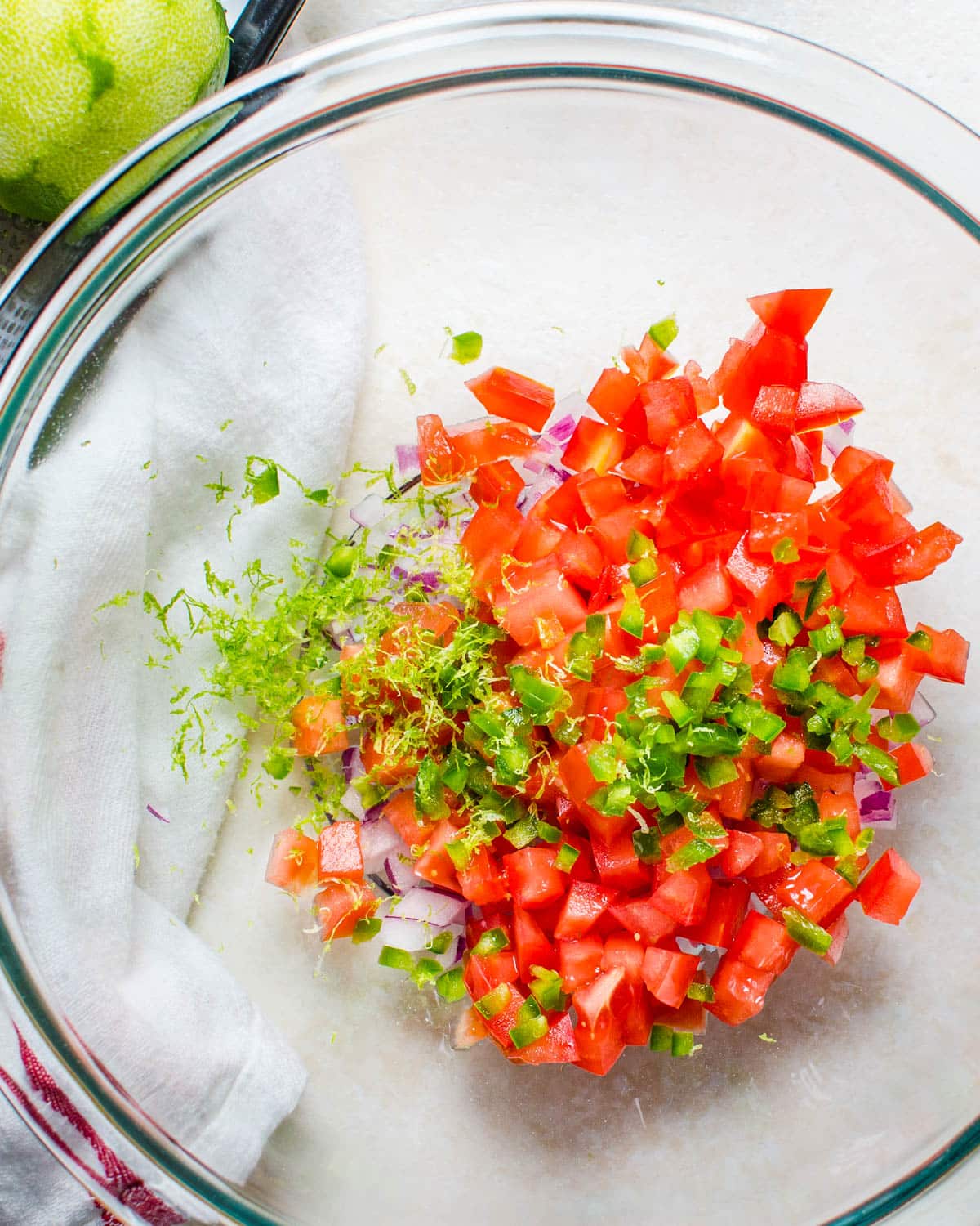 I am combining red onion, jalapeno, lime zest and diced tomatoes in a bowl.