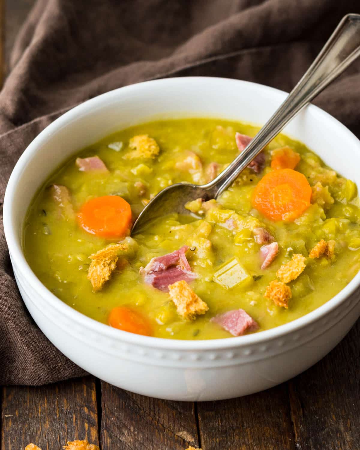 A larger bowl of soup with chunks of ham and carrots. 