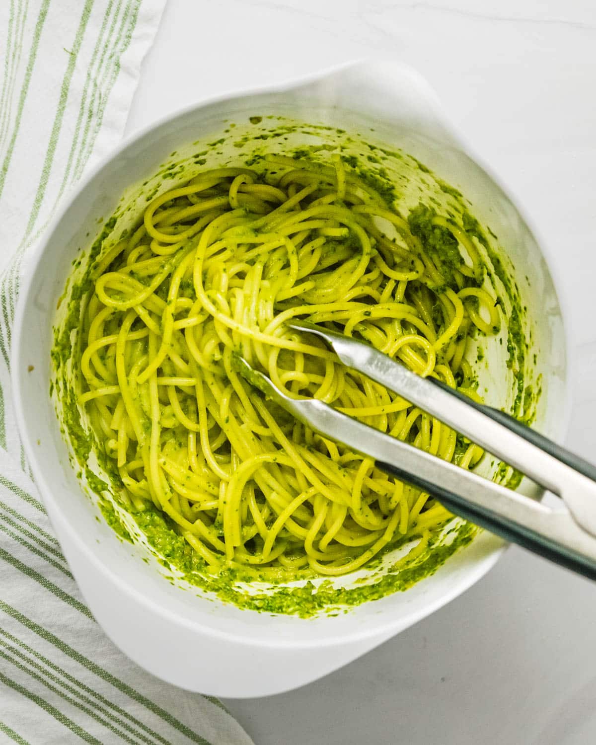 Mixing cooked pasta with the pesto until it's well coated. 