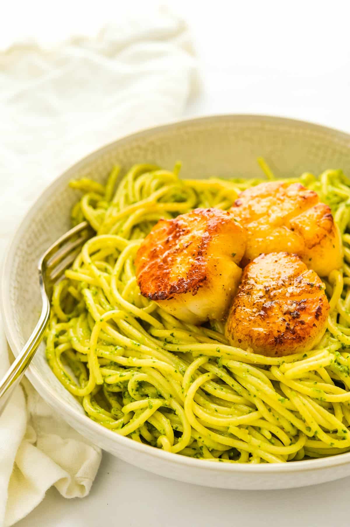 Topping a plate of pasta with seared sea scallops.