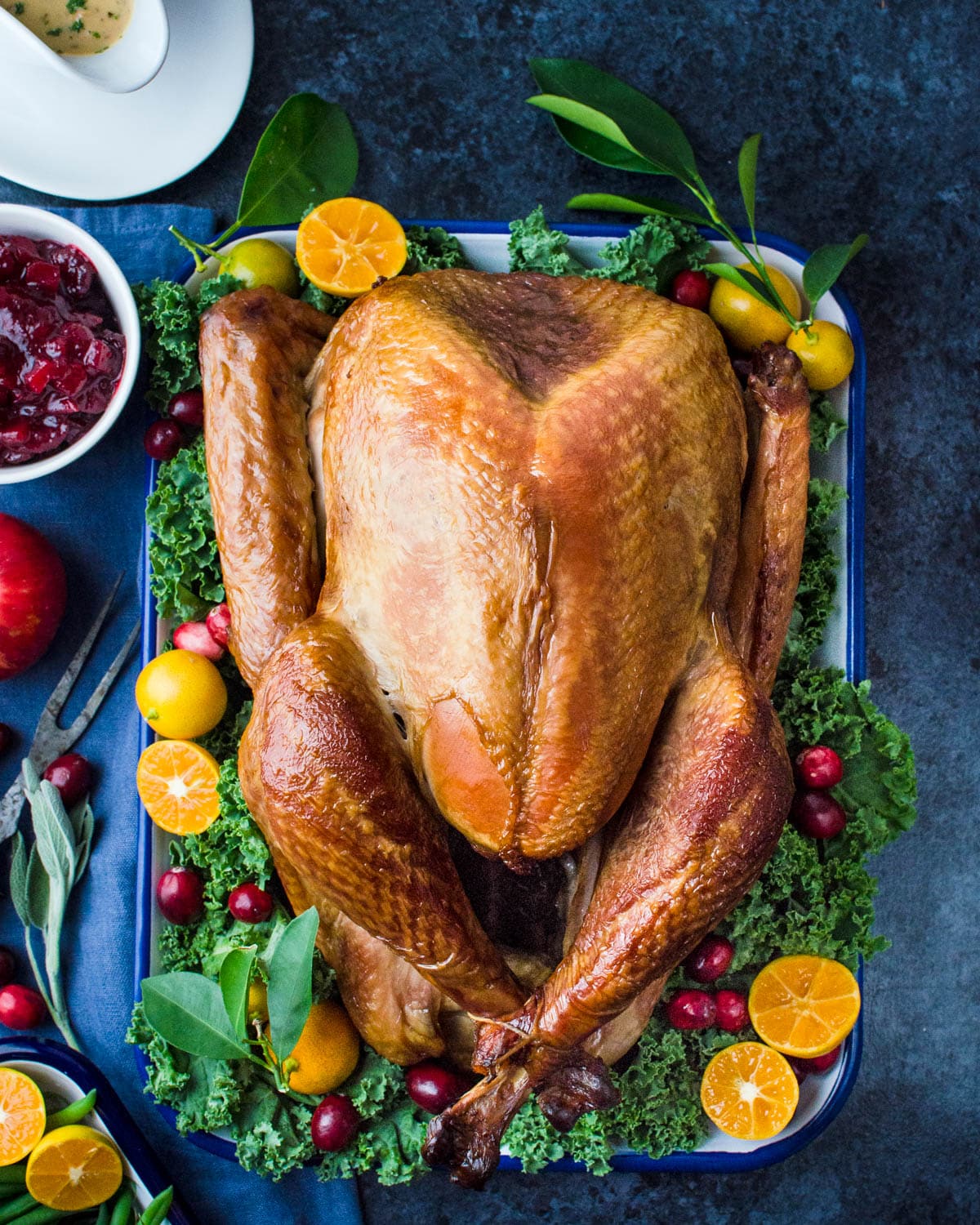 A white platter laden with greenery, fruits, and the whole smoked turkey as the centerpiece.