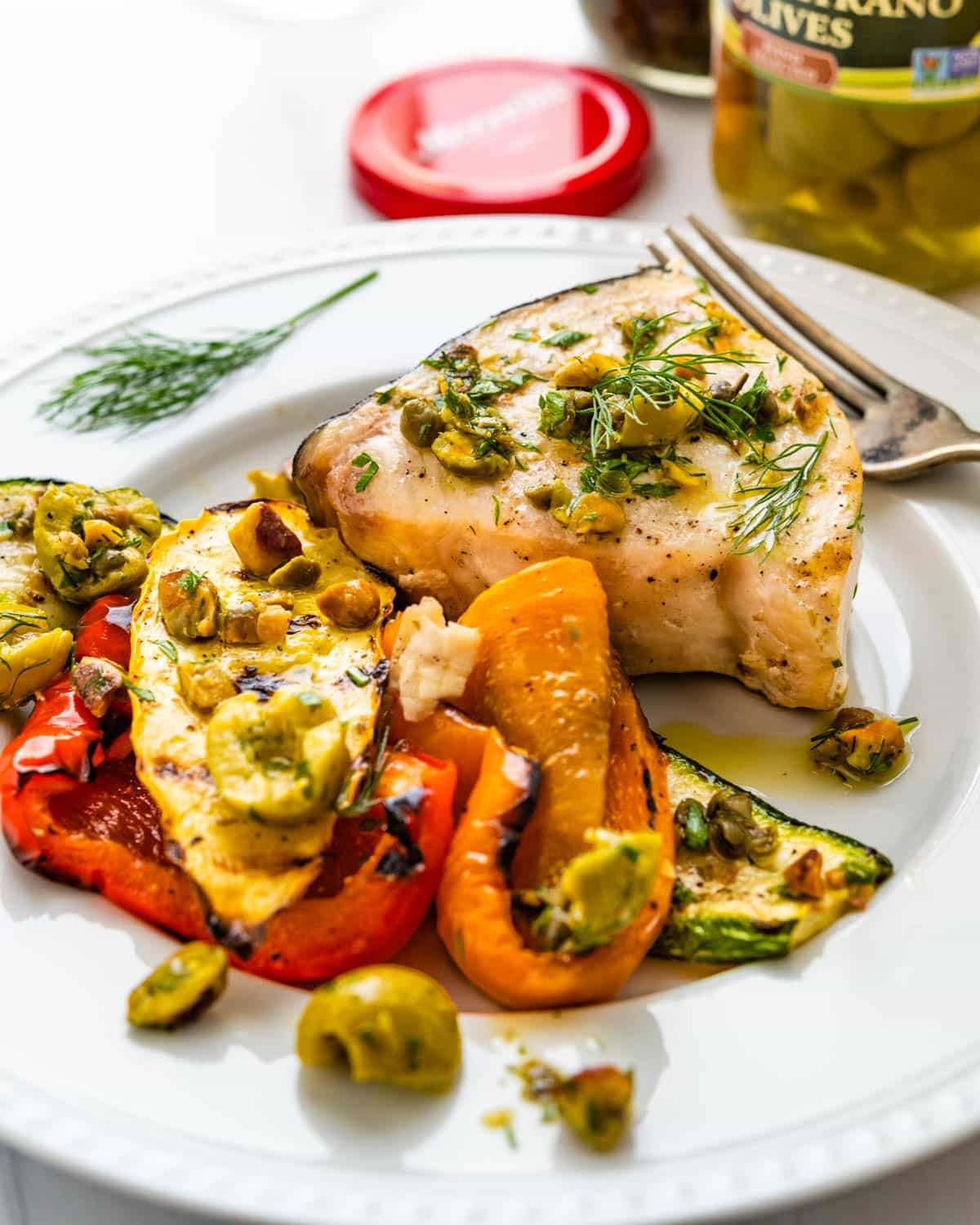 A plate of grilled swordfish and vegetables with olive pistachio relish.