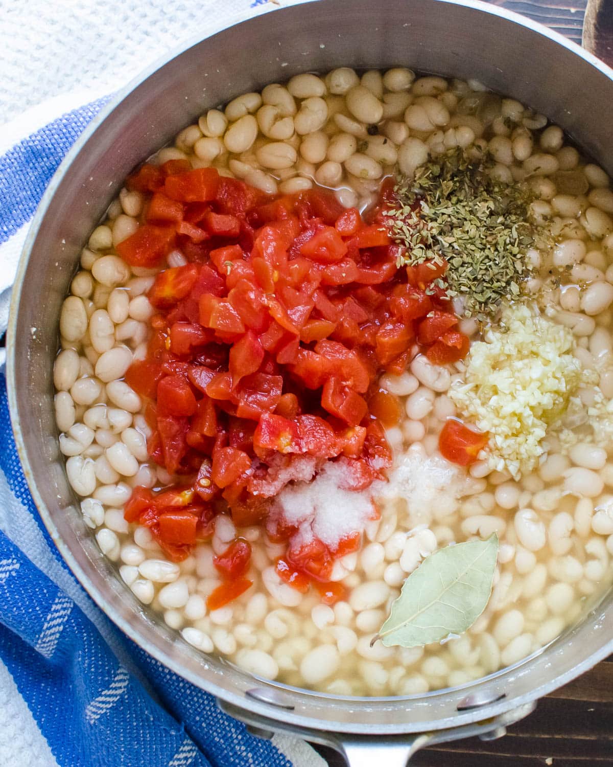 Adding canned tomatoes, garlic and oregano to the white beans.