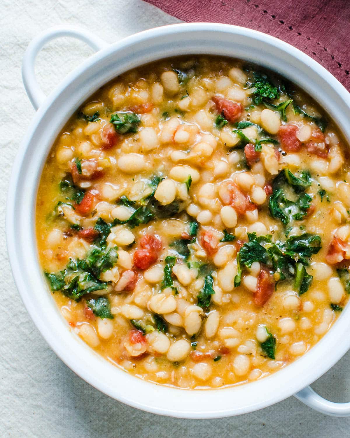 A dish filled with the stewed white beans, kale and tomatoes. 
