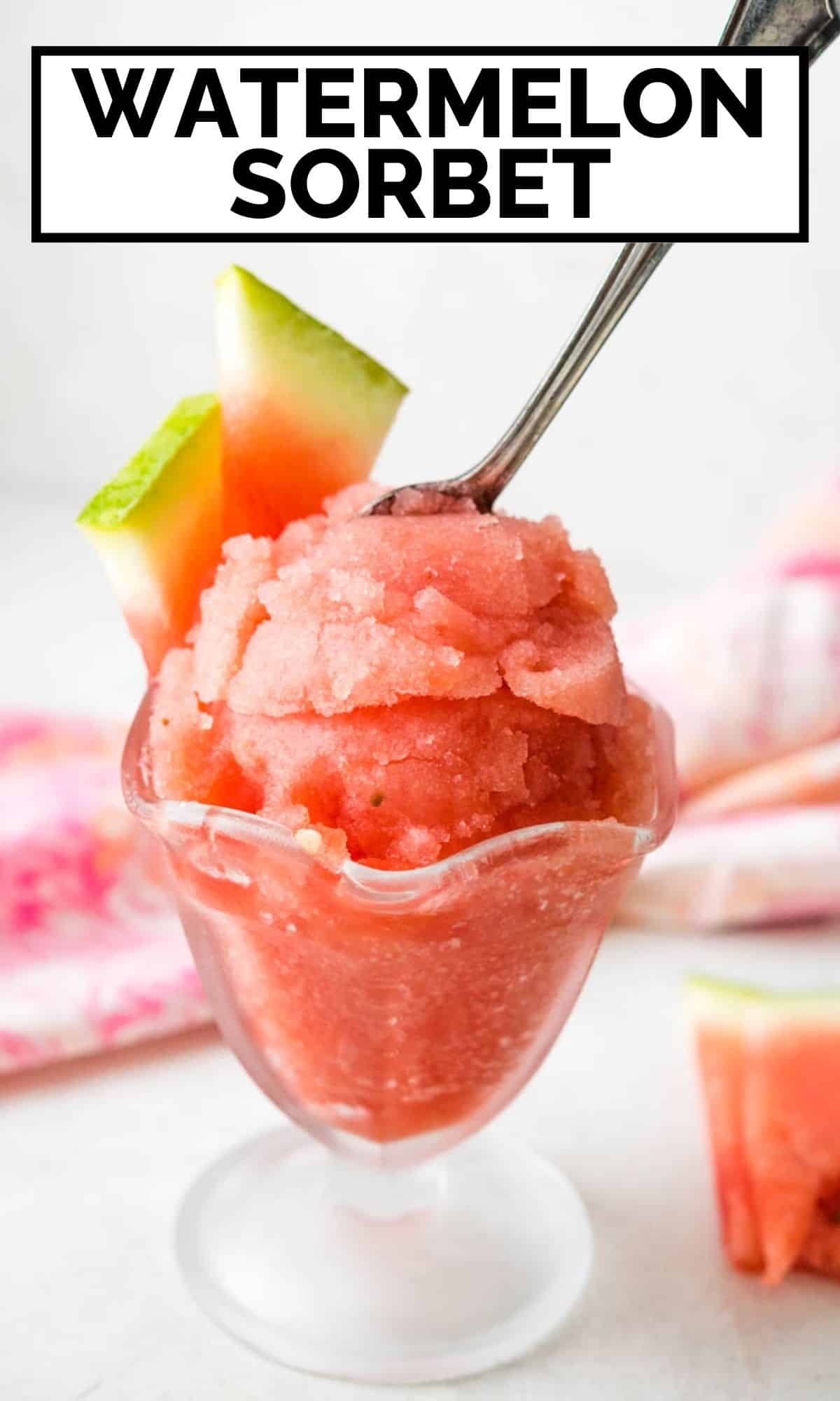 A dish of watermelon sorbet with a spoon and slice of fresh fruit.