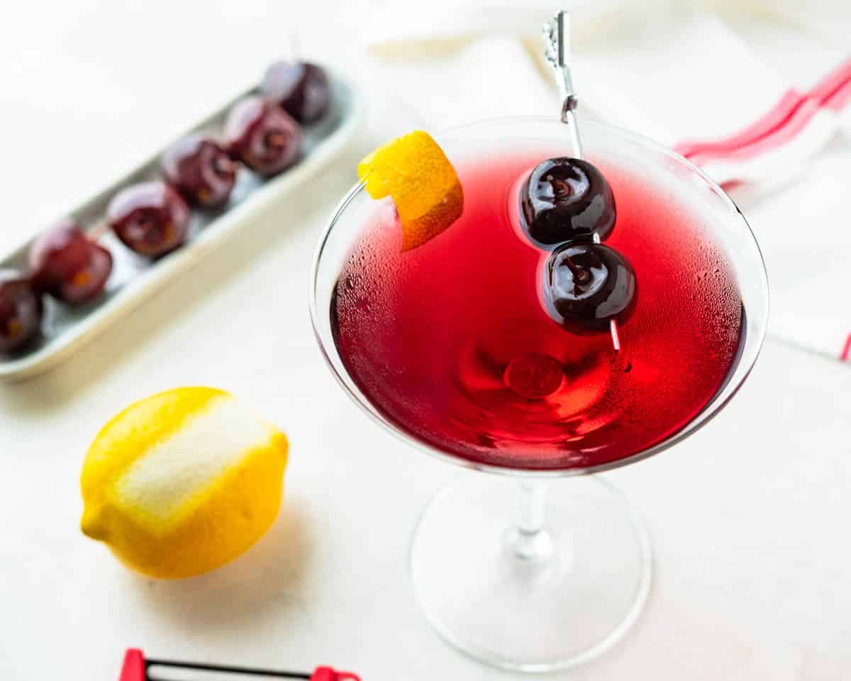 A cherry martini with lemon and cherry garnish.