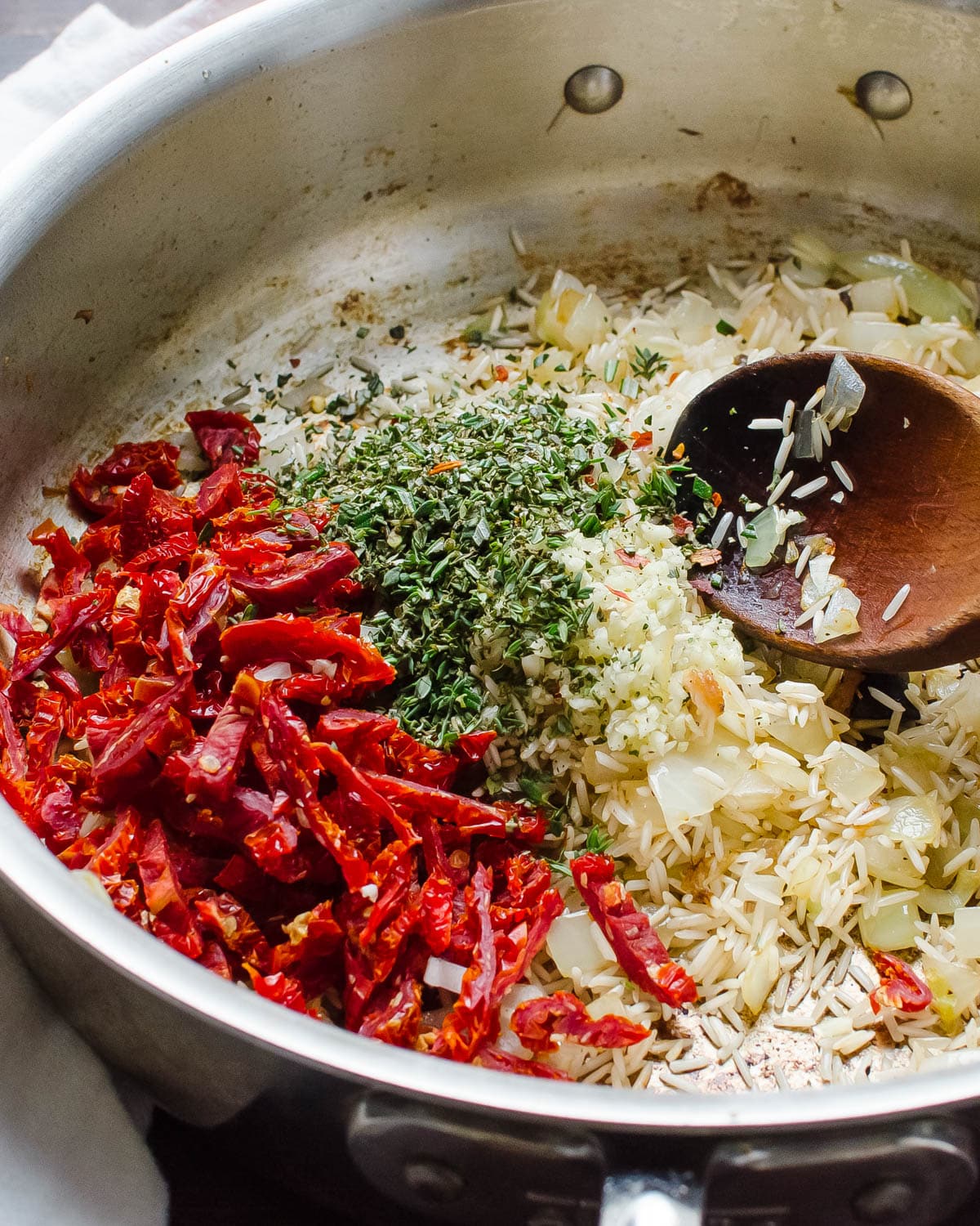 Adding chopped herbs and sun-dried tomatoes to the rice mixture.