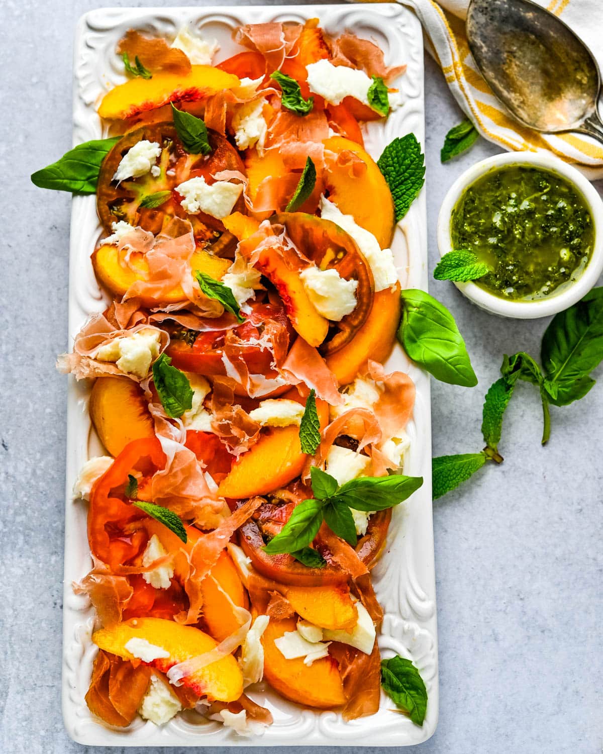 a platter of tomato peach caprese with herb sauce on the side.