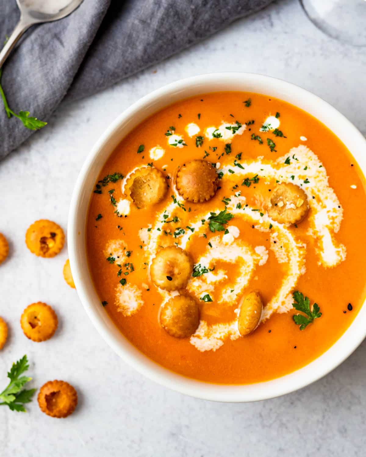 Creamy bell pepper and tomato soup in a white bowl with garnishes. 