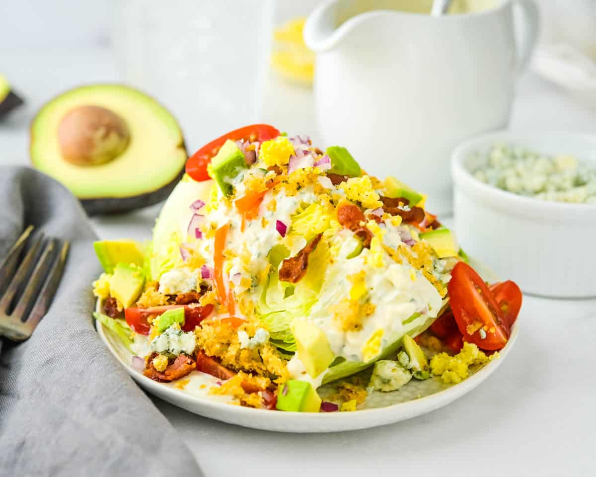A wedge salad with croutons, avocado, bacon, tomato, carrots and blue cheese crumbles.