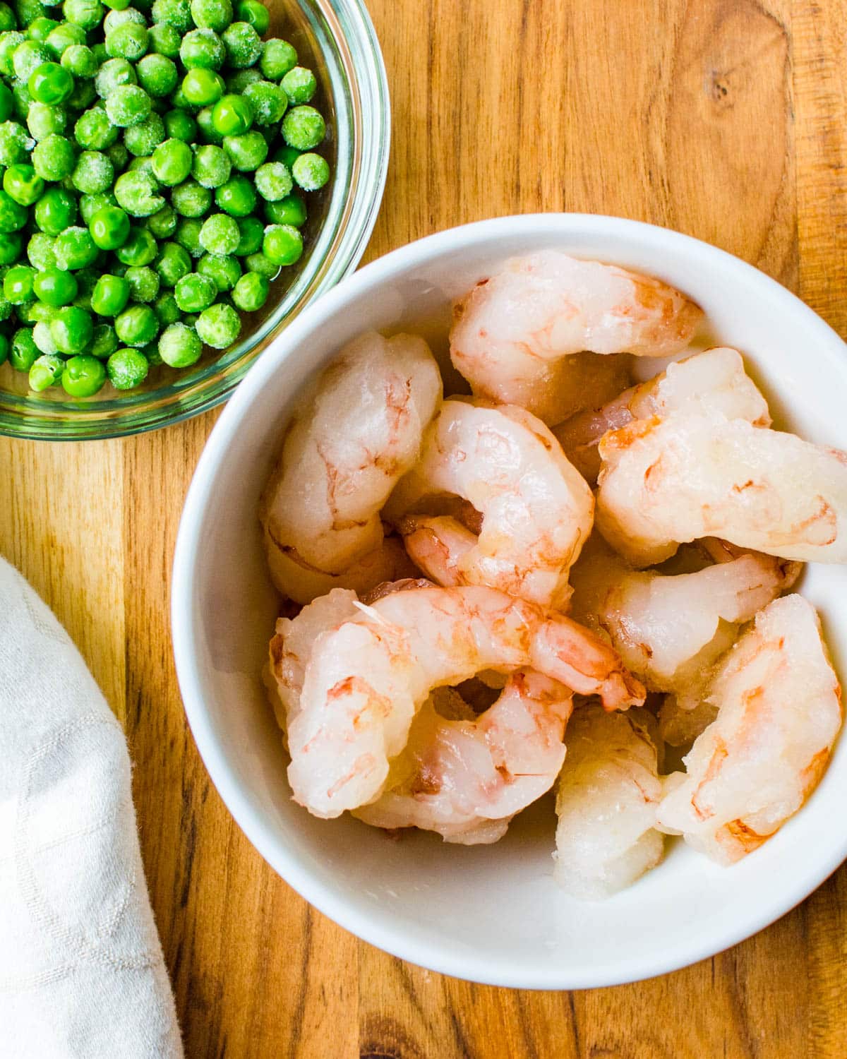 Peeled and deveined shrimp and a bowl of frozen peas.