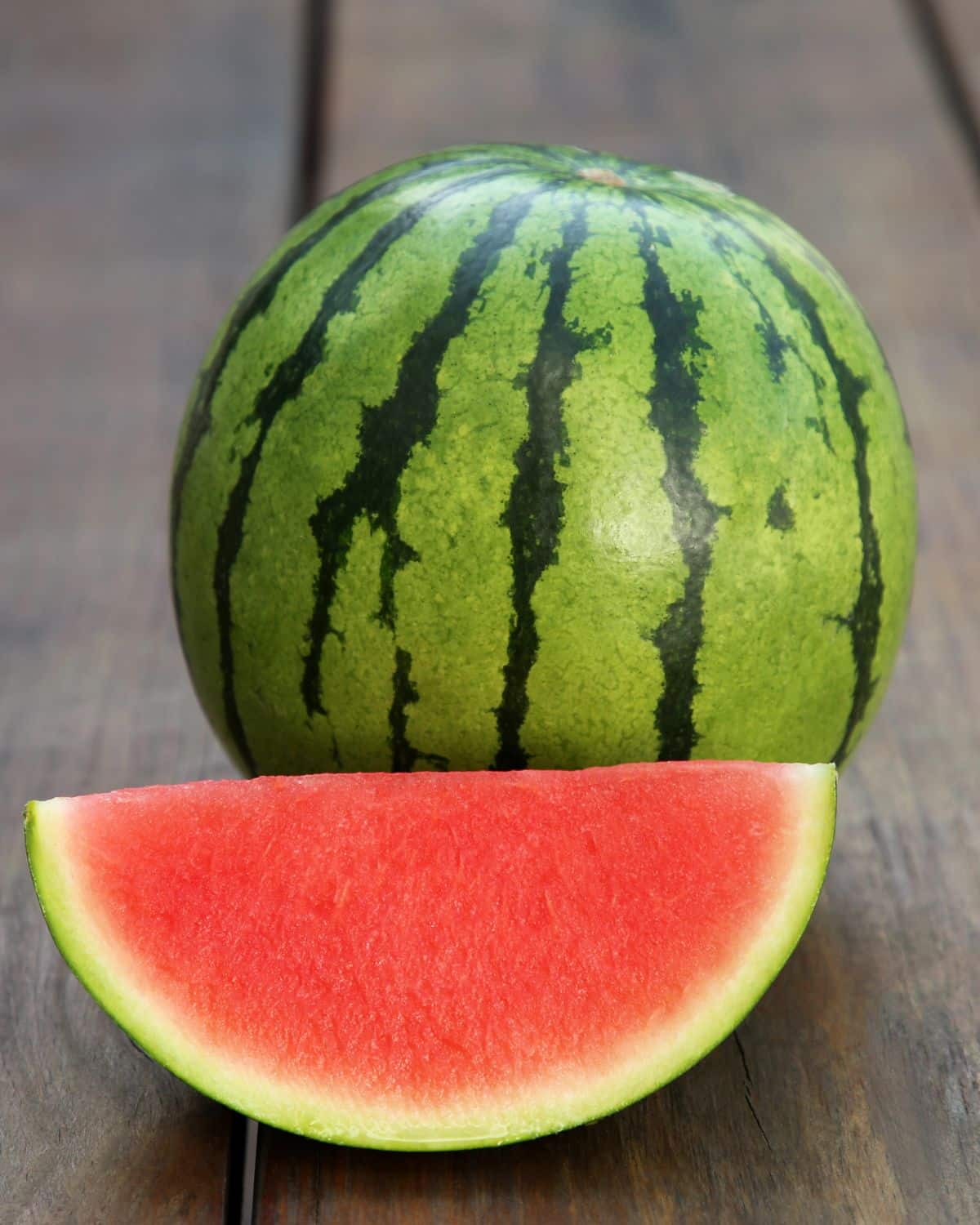A whole watermelon with a wedge of watermelon next to it.