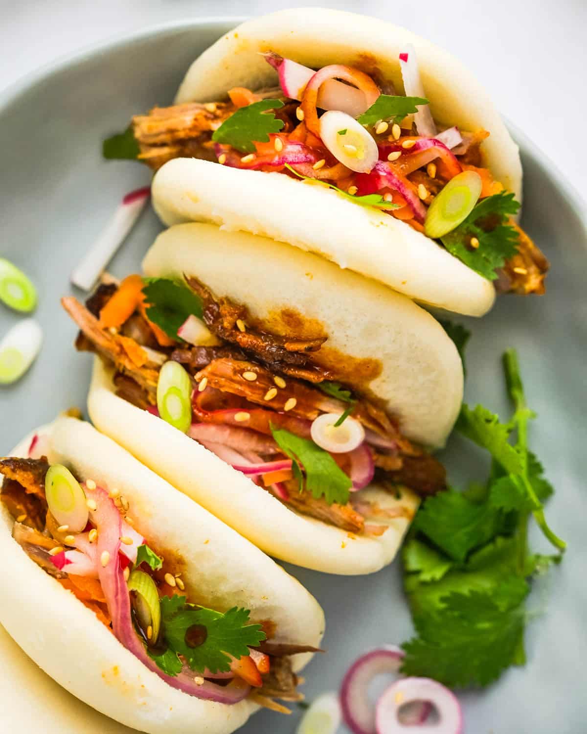 A plate of BBQ pork bao buns with toppings.