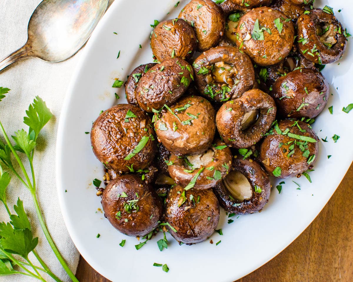 A side dish of balsamic dijon roasted mushrooms with a serving spoon.