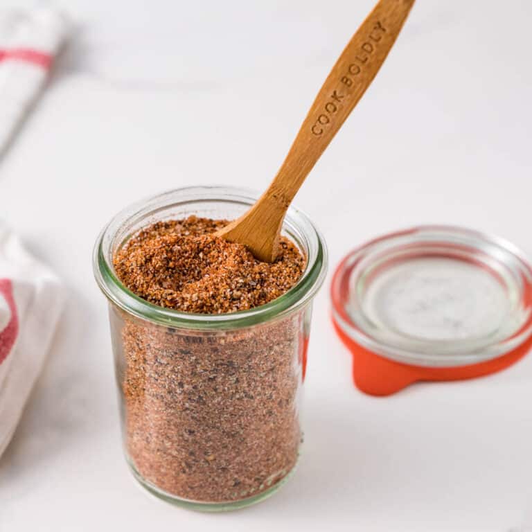 A jar of bbq rub with a spoon for scooping.
