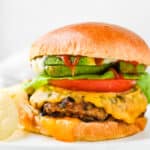 Chicken burgers on a brioche bun with cheese, lettuce, tomato and avocado.