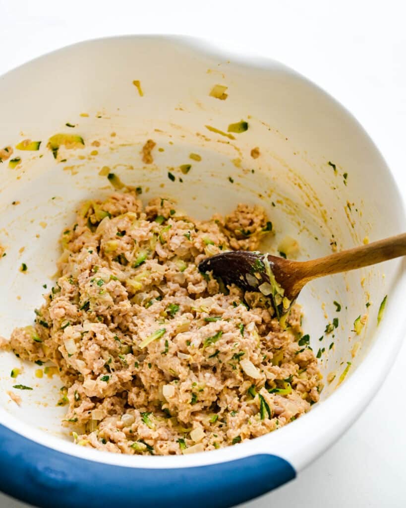 Mixing the ground chicken mixture in a large bowl with a wooden spoon.