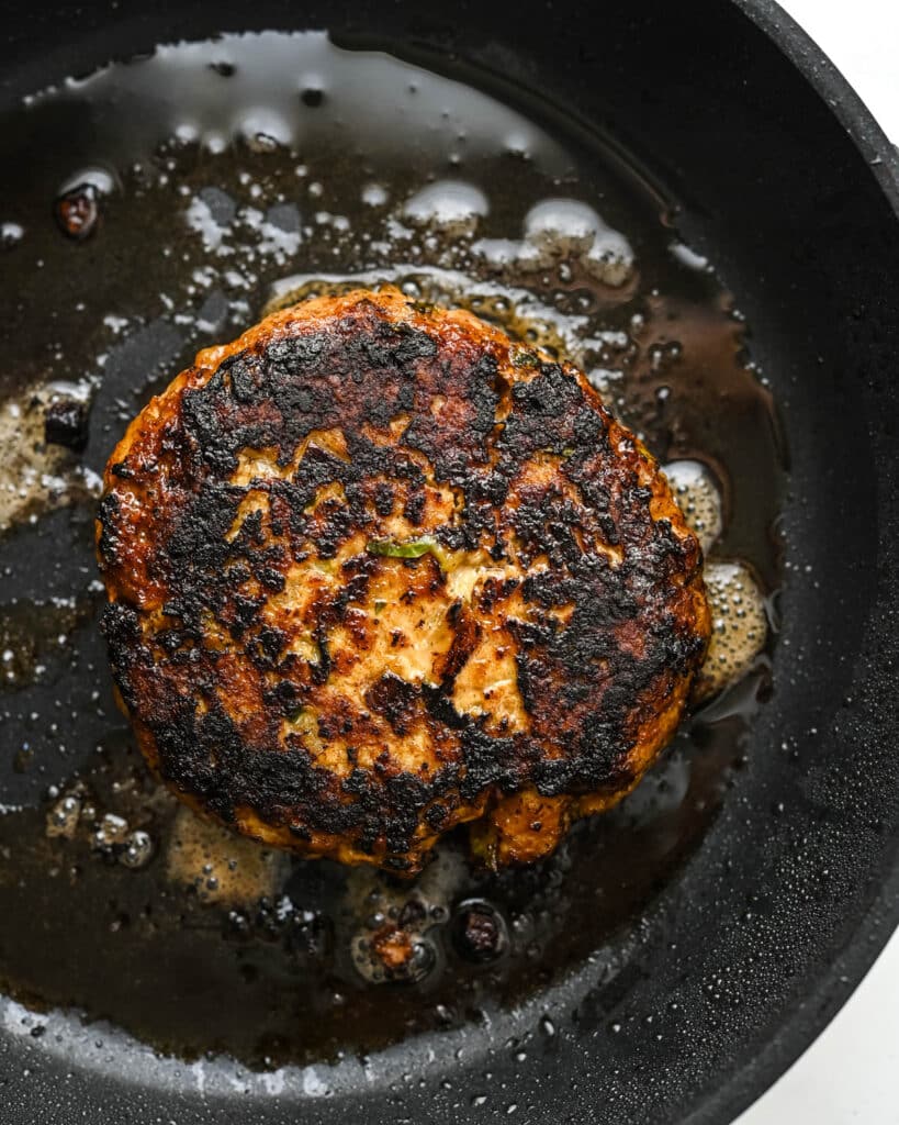 Frying the ground chicken patties in hot oil in a skillet.