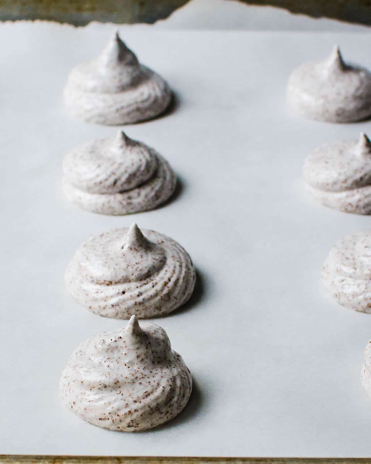 Meringues piped onto a parchment-lined sheet pan.