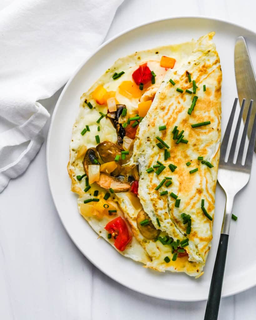 Serving a veggie filled egg white omelet on a white plate with fork and knife.