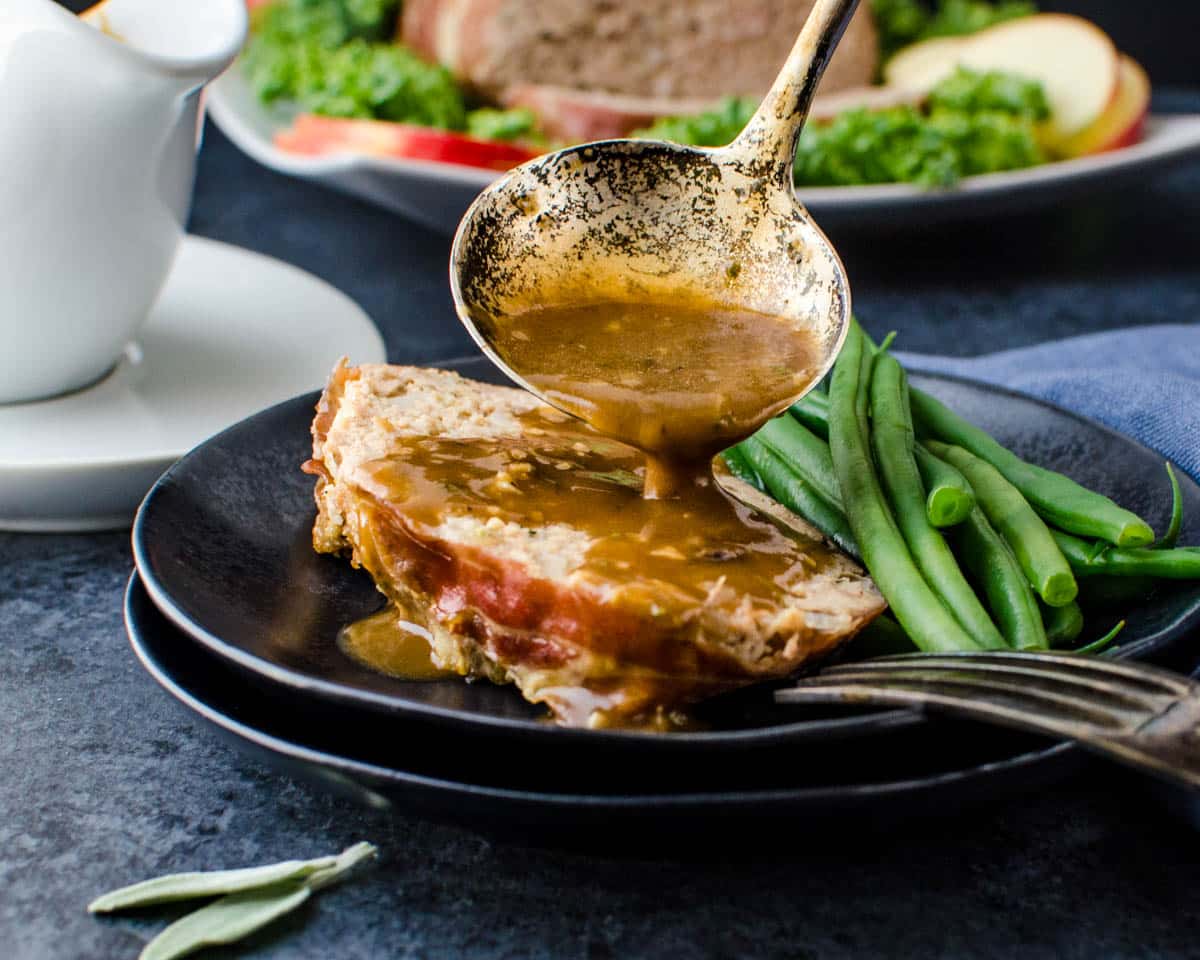 A slice of meatloaf is topped with the gravy.
