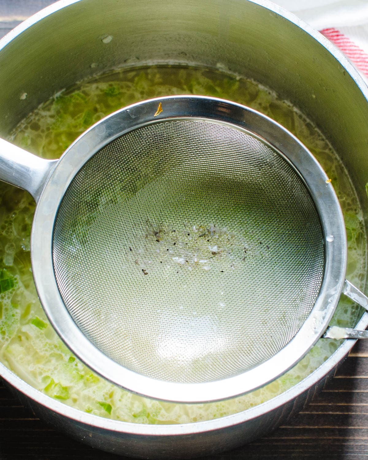 Straining oyster liqueur into the vegetables.