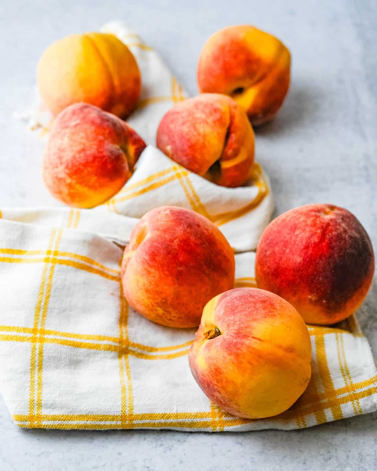 Seven fresh peaches on a dish towel.