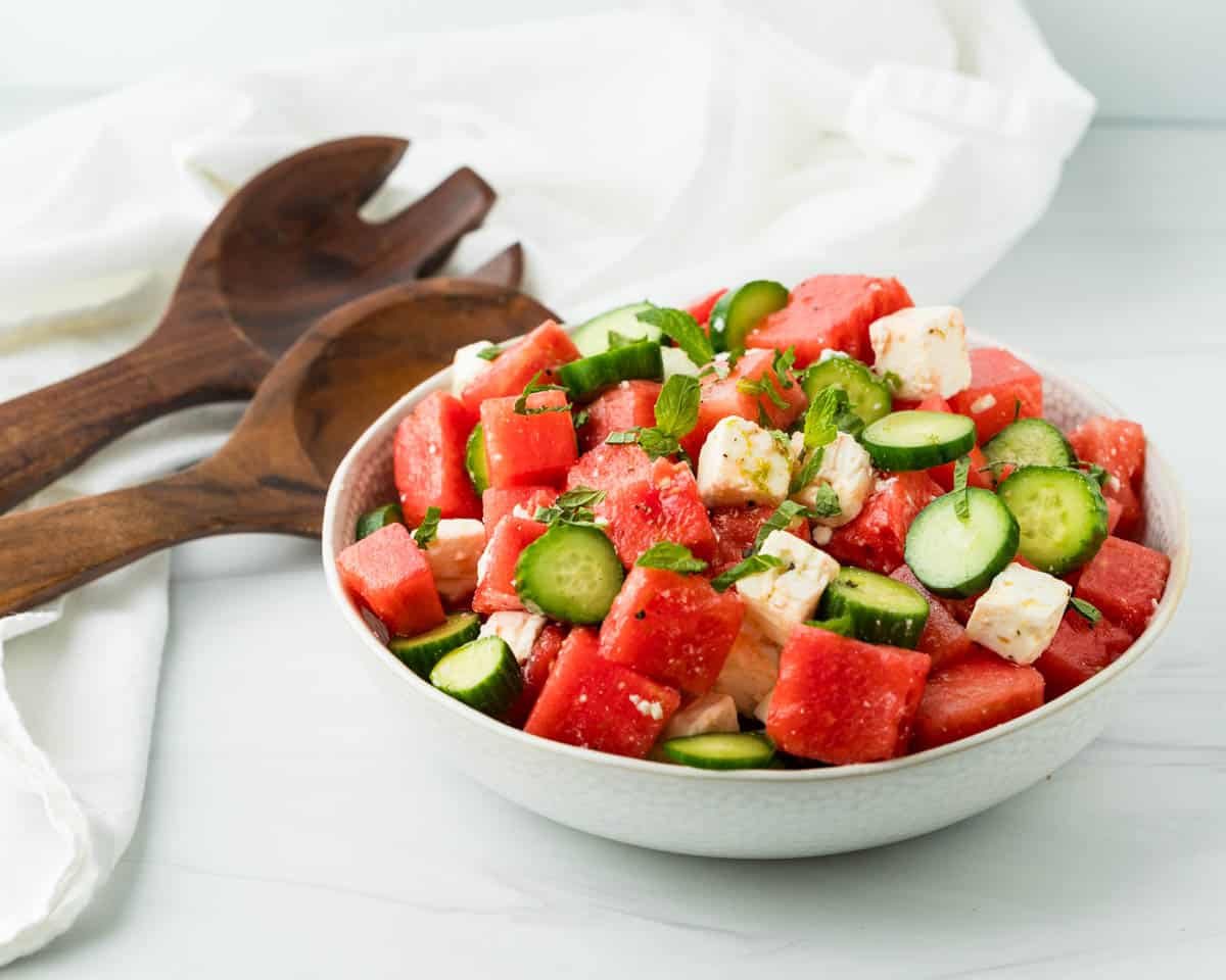 Serving the watermelon cucumber salad in a white serving bowl with fresh mint leaves.