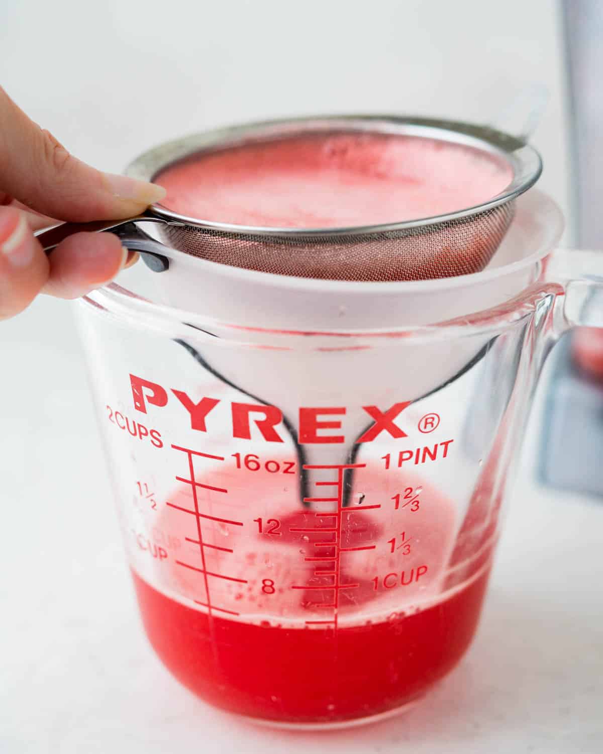 Straining watermelon juice through a mesh strainer into a glass measuring cup.
