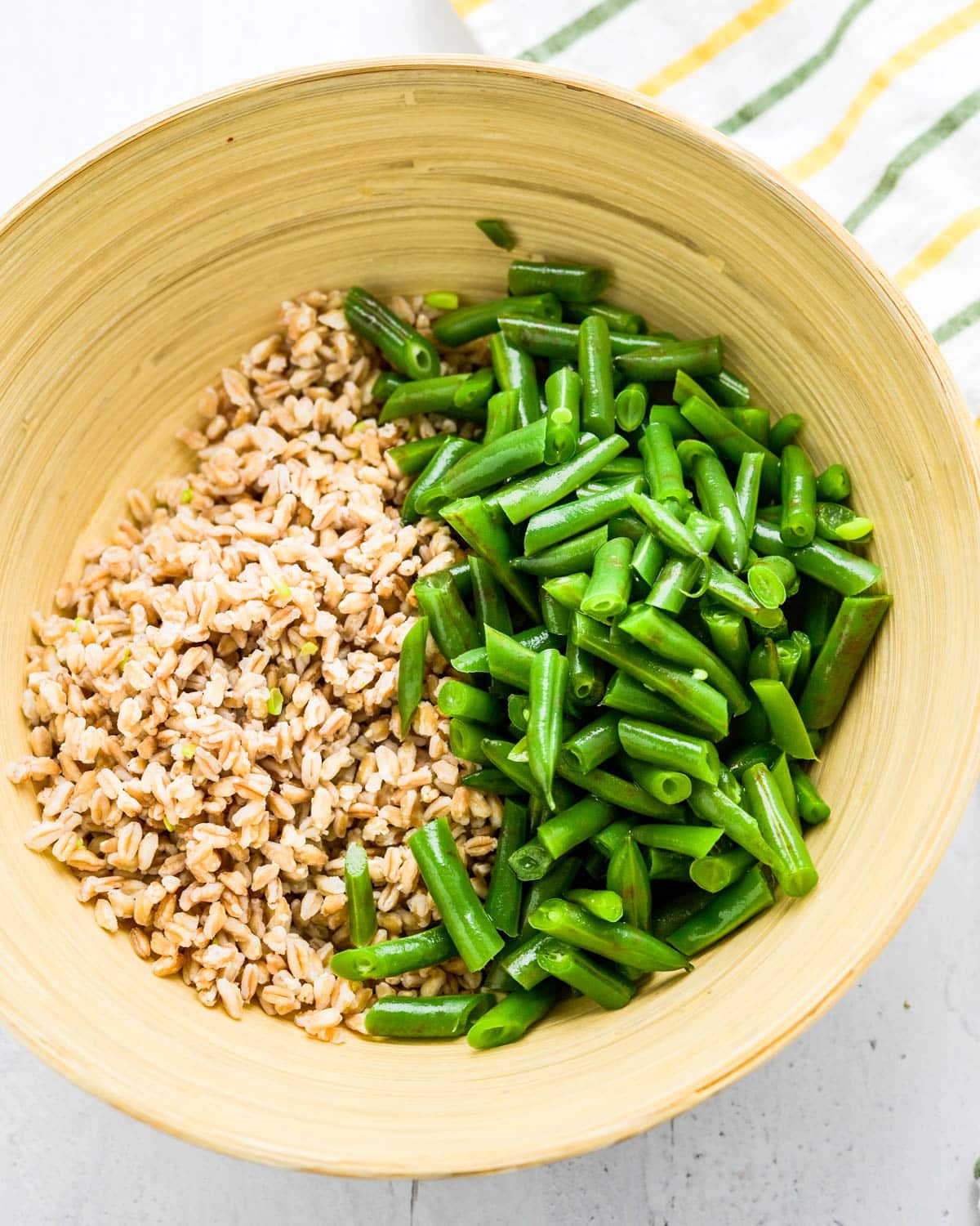 combining the cooked farro and green beans in a salad bowl.