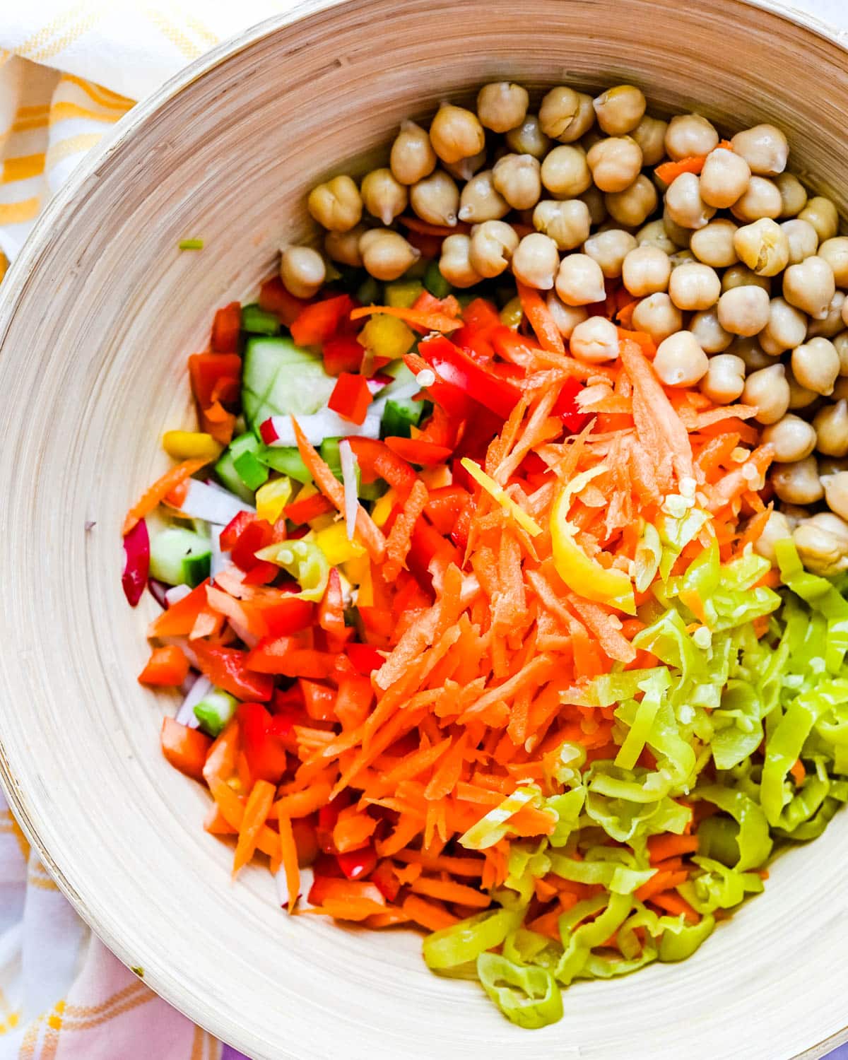 adding carrots, garbanzo beans, bell peppers and pepperoncini to a large bowl.