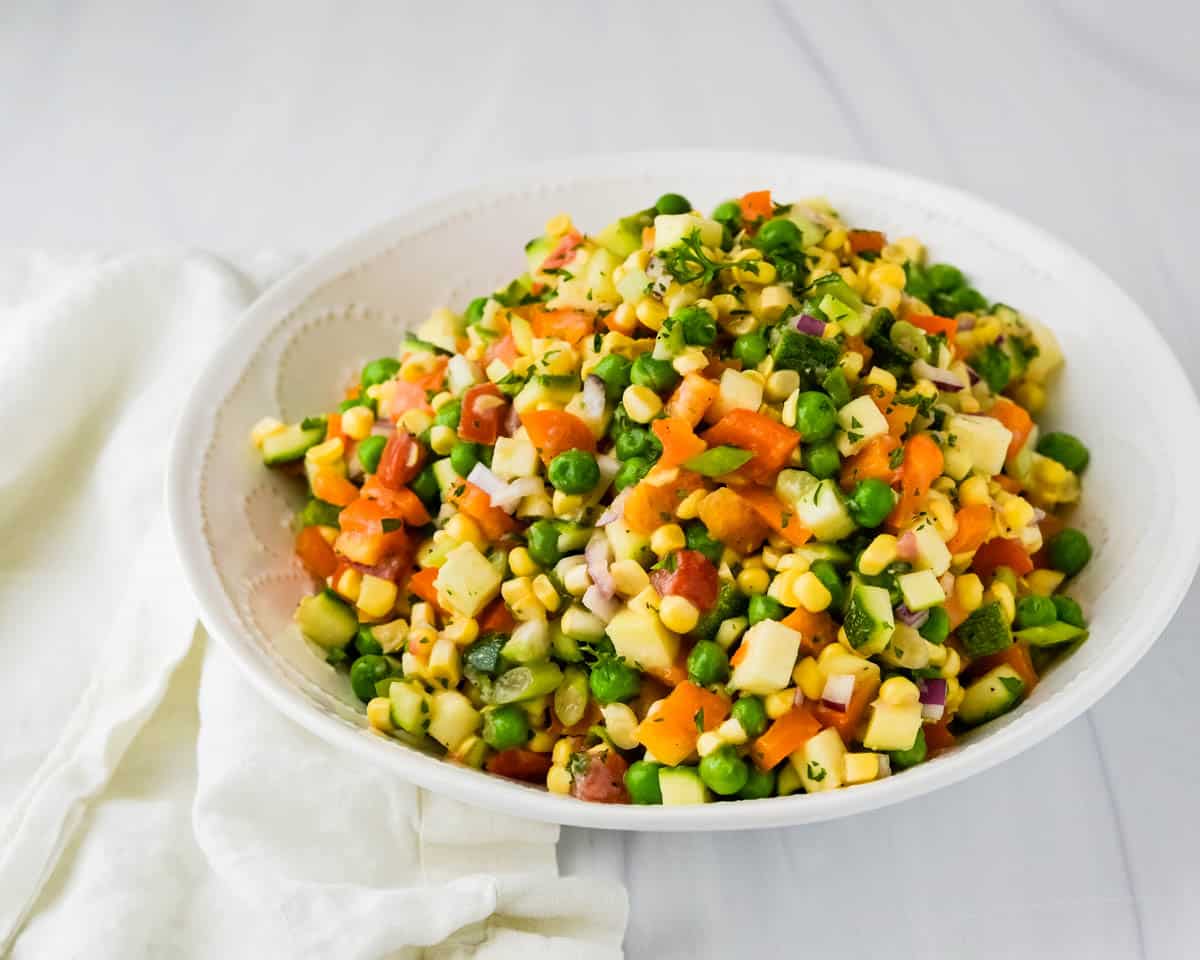 Serving the corn zucchini and bell pepper salad with peas in a white bowl.