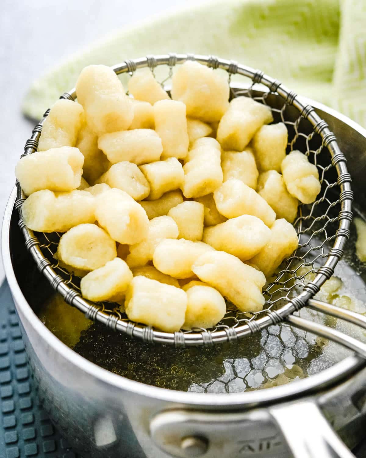 Cooked gnocchi being scooped from boiling water with a kitchen spider.